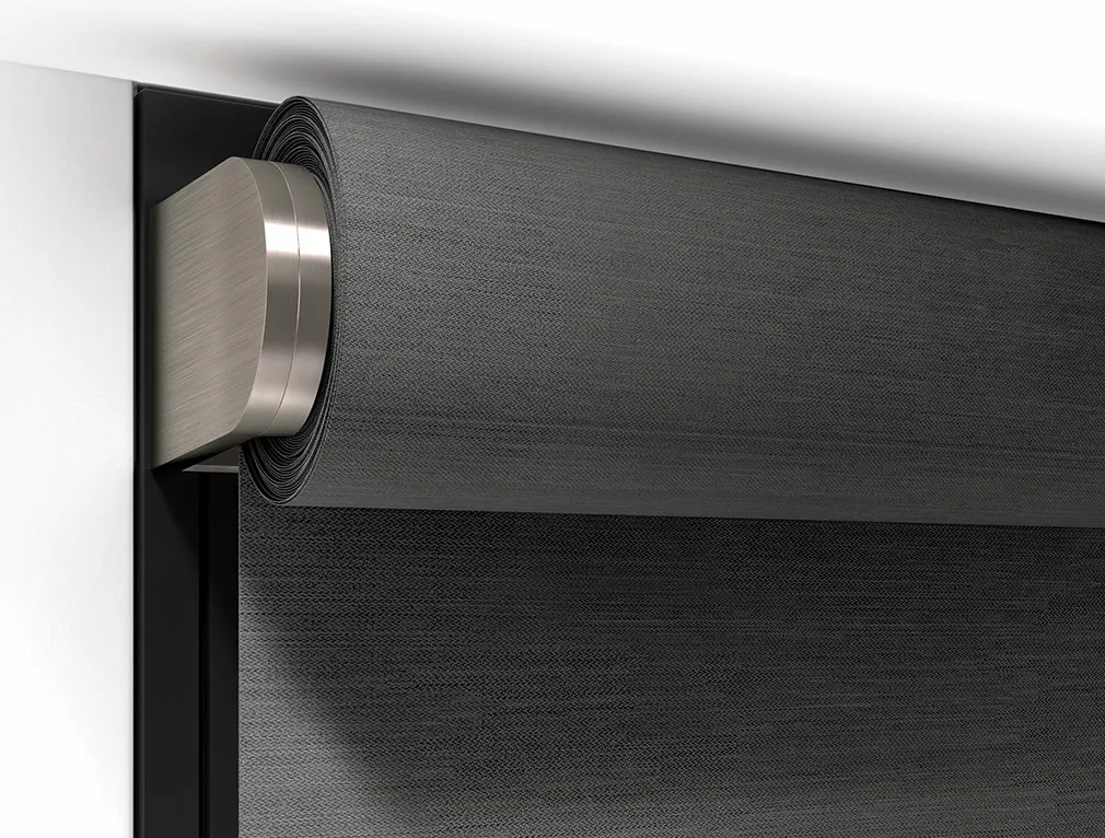 Close-up detail of a motorized roller shade with dark charcoal woven fabric and a brushed nickel endcap, outside mounted at the window frame